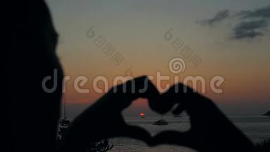 年轻女子在海滩日落时用<strong>双手</strong>制作心脏<strong>标志</strong>剪影。 泰国普吉岛。 4K.